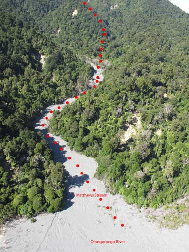A red dotted line extends up through a photo of a dry river bed towards a peak out of frame.