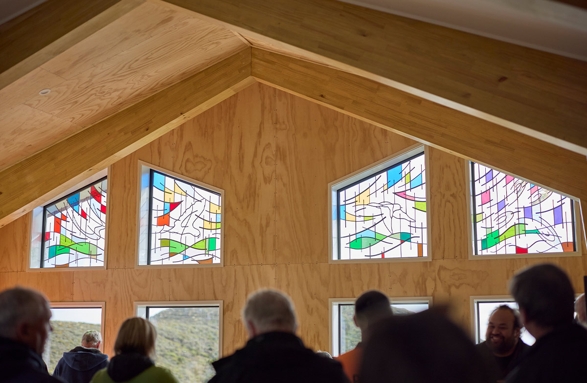 People sit in a ply lined hut that has high stain glassed windows.