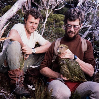 Two men, one holding a kakapo. 