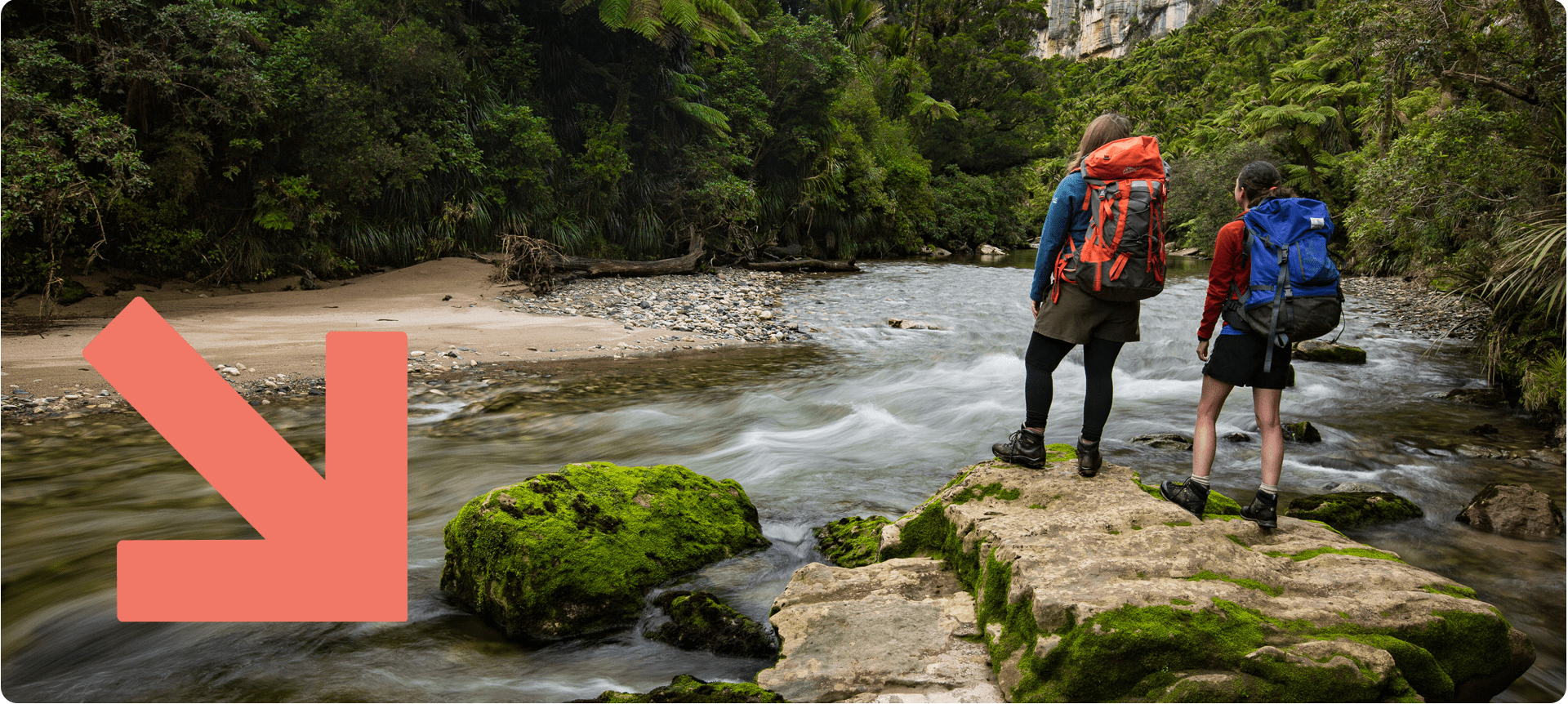 2 hikers standing on a large rock at a river on the Paparoa Track.