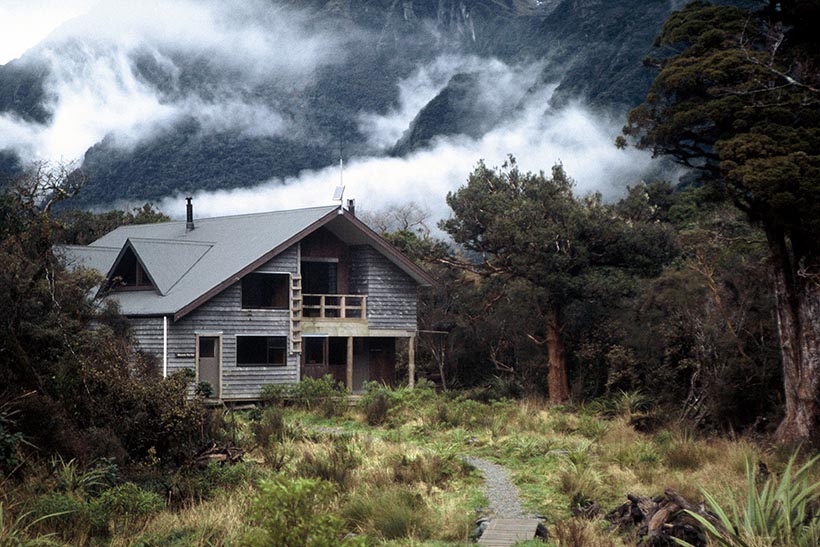 Large wooden hut positioned at the foot of mist-clad wooded hills.