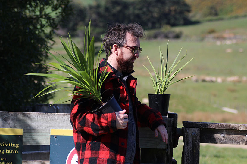 Man leans against a fence while holding a potted plant width=