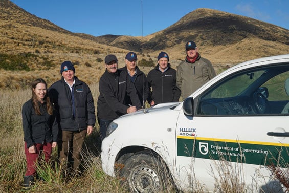 Fulton Hogan and DOC signing agreement on car bonnet in field.