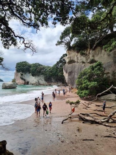 Groups of people walking along a cliff-hugging beach. 