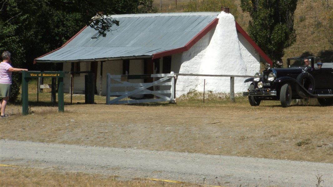 Molesworth cob cottage with people and vintage car in the foreground.