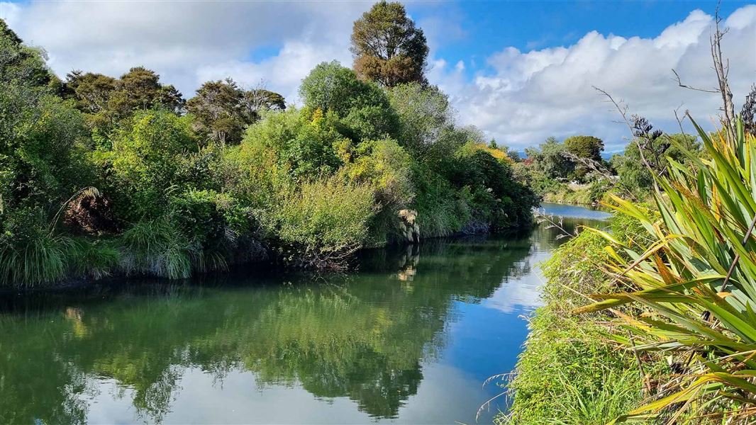 A flat calm narrow river  with foliage wither side, reflecting the blue sky, clouds and trees.  