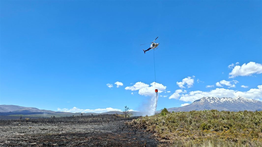 Helicopter fights vegetation fire dropping water from a bucket with Mt Ruapehu in the background. 