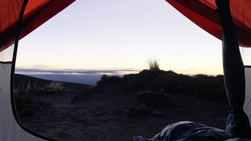 View from inside a red and cream tent out to a volcanic landscape.