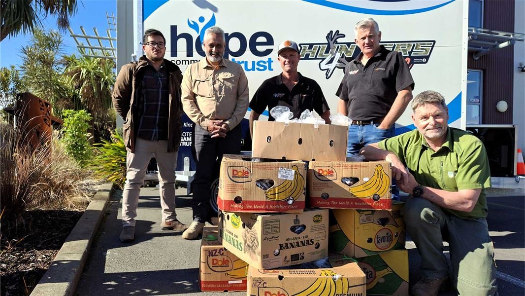 Five men posing  in front of a truck, with a stack of banana boxes filled with bagged venison. 