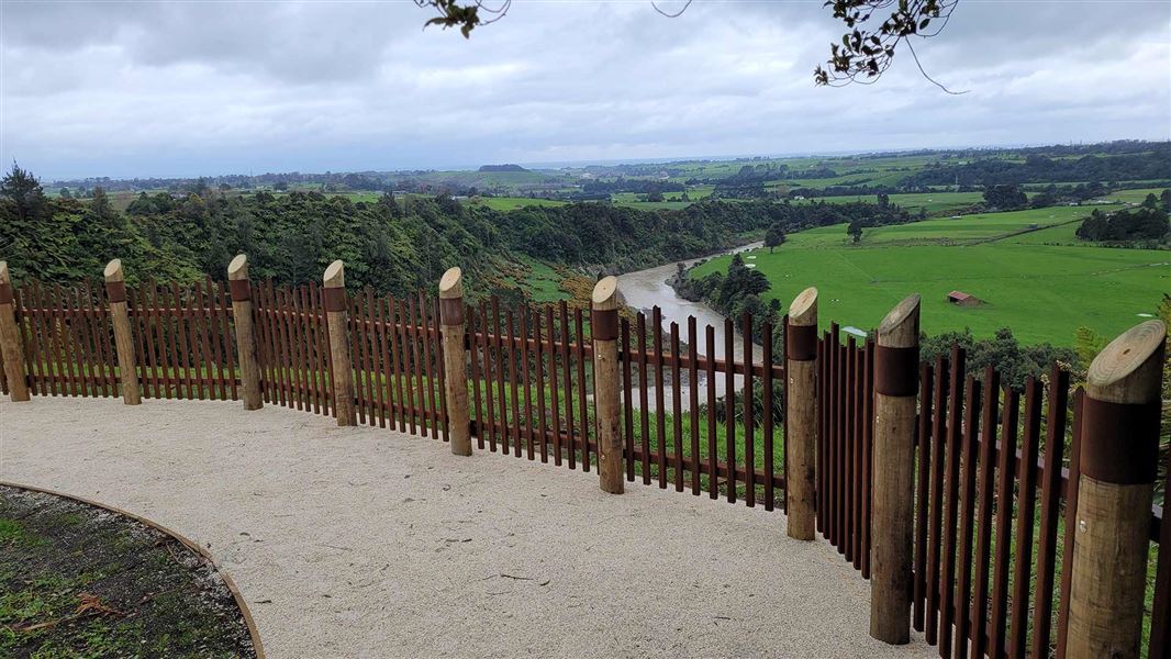 View from a fenced platform overlooking green hilss and a curling river below. 