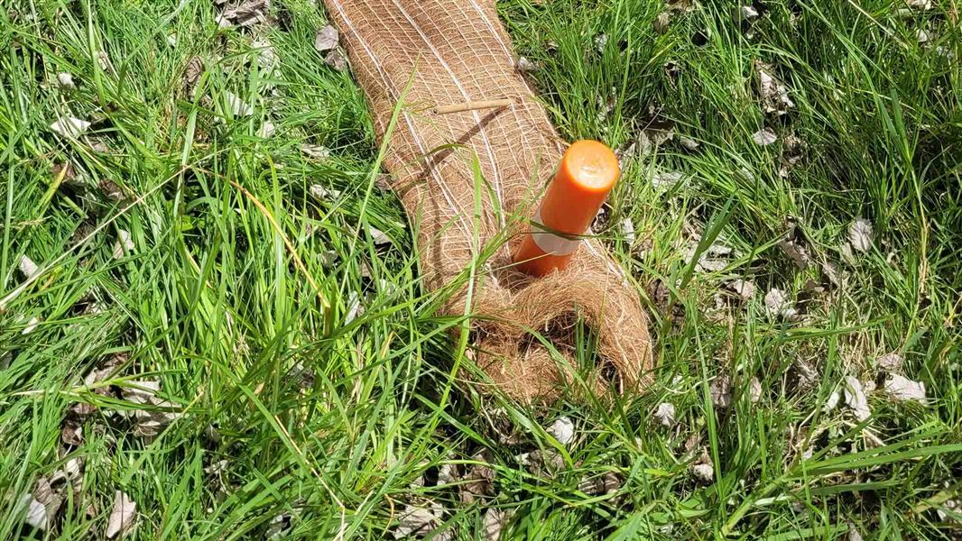 A mat made from coconut fibres lies in the grass beside a river.