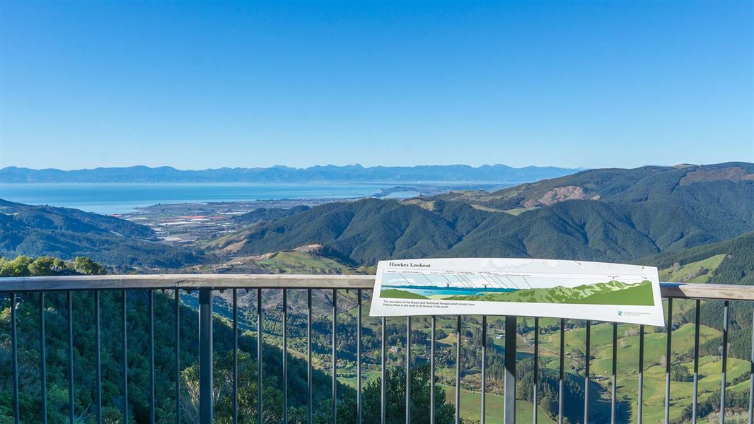 View over a valley and out to seas, with a balustrade and interpretation panel in the foreground.