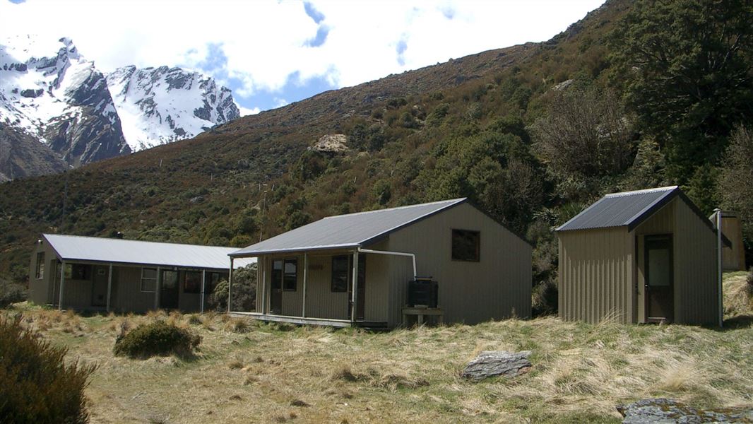 Three small buildings set in a mountain backdrop. 