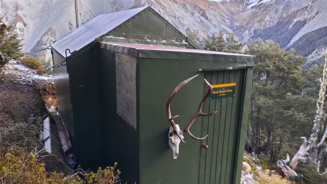 A small wooden hut painted green perched on a hillside.