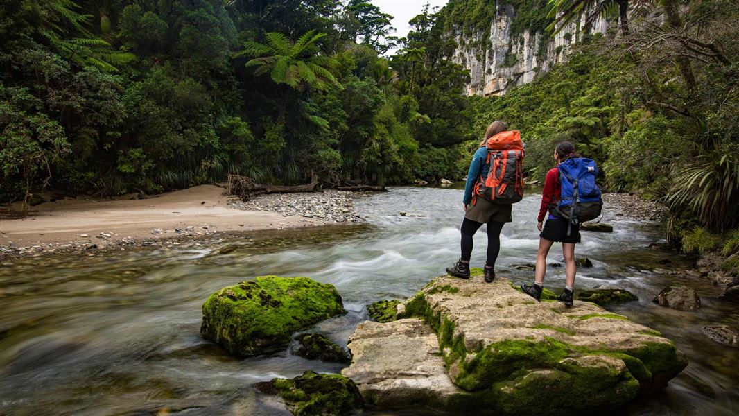 Two people standing by a river surrounded by bush