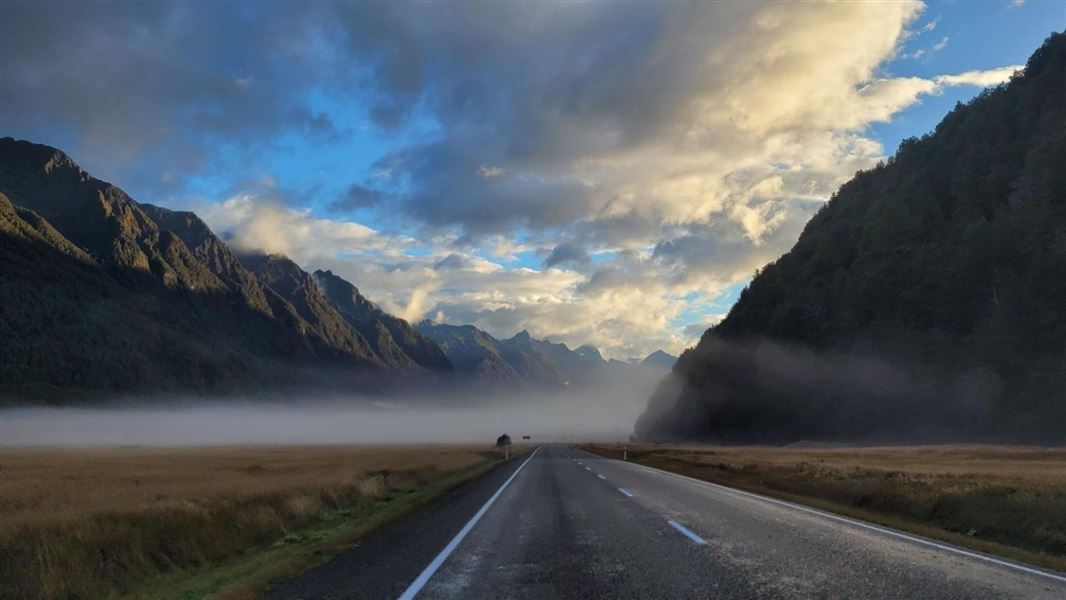 A road disappears into the mist at the bottom of a mountain valley.