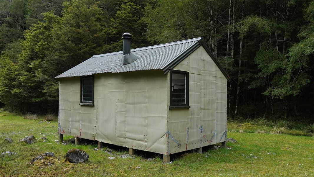 A small beige hut clad in metal with a maroon roof. 