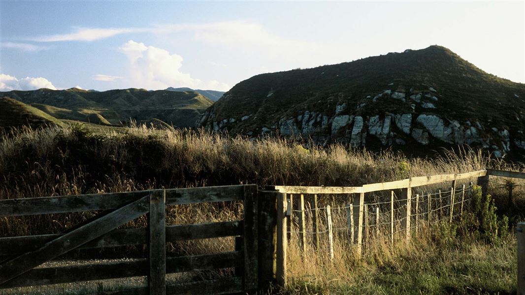 View of a fence and gate, with steep hills in the background.