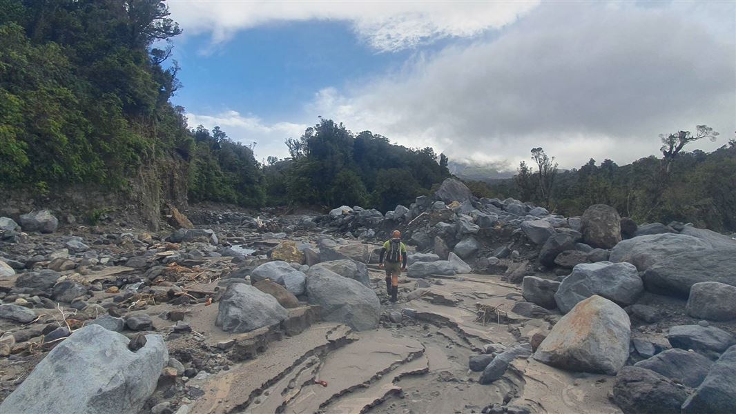 A person walks over a rocky outcrop towards the bushline. 