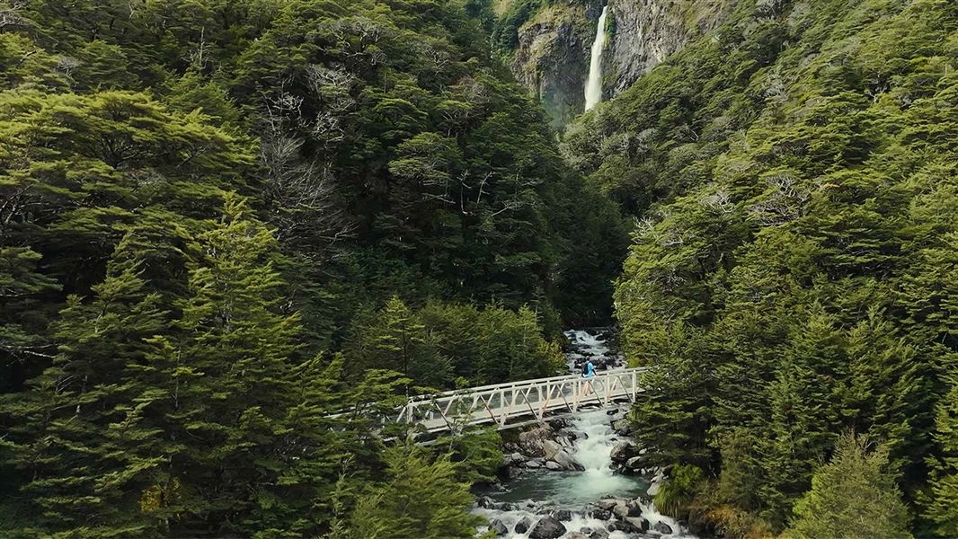 Poeple walking across a bridge over a river with waterfall in background. 
