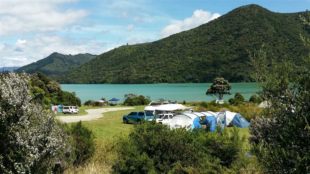 Rolling green hills, with a large body of clear water and a camp of tents at the base.
