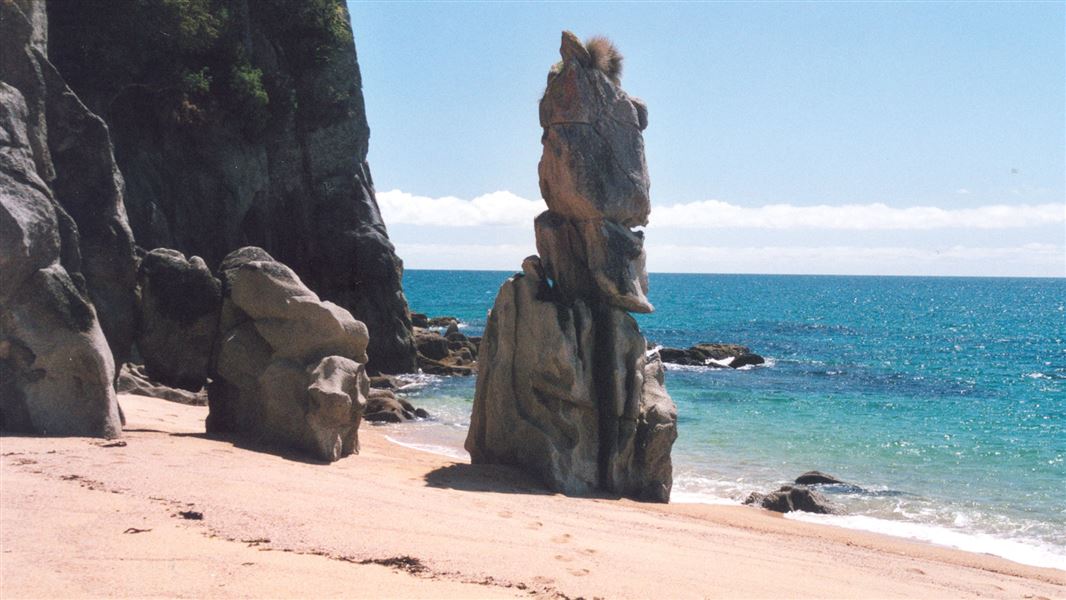 Weather sculpted rocks loom out of the golden sand by the sea.