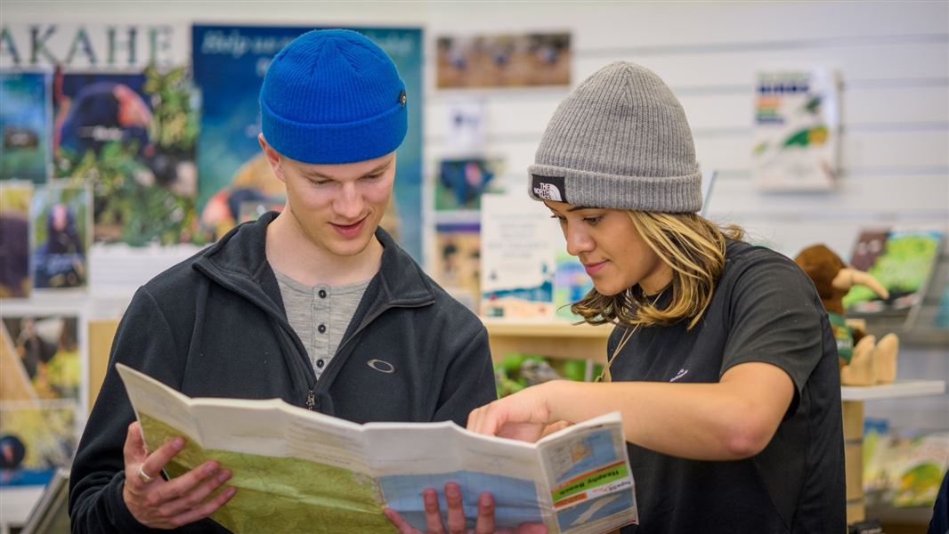 Two people reading a map in a DOC Visitor Centre.