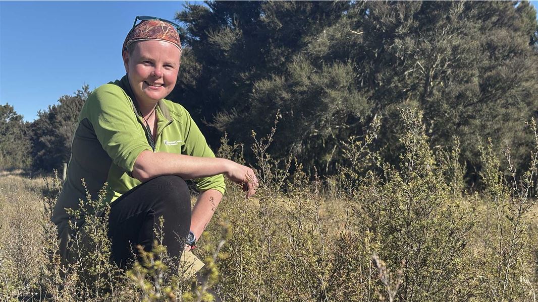 A smiling person crouching in a meadow with trees in the background.