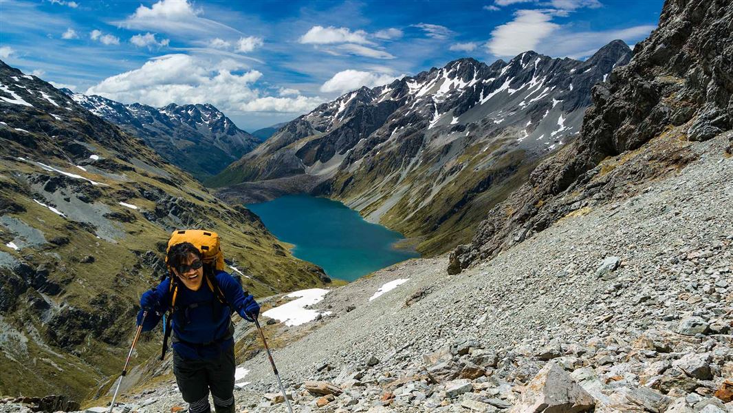 Tramper on steep shingle way above the lake behind. 