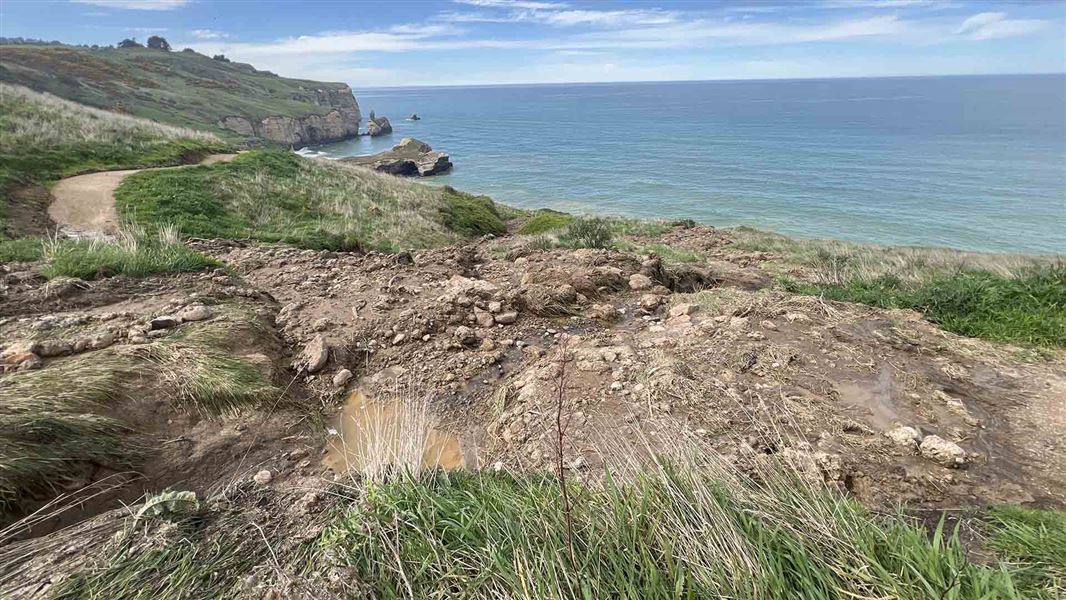 A patch of muddy ground on a cliff above the ocean.