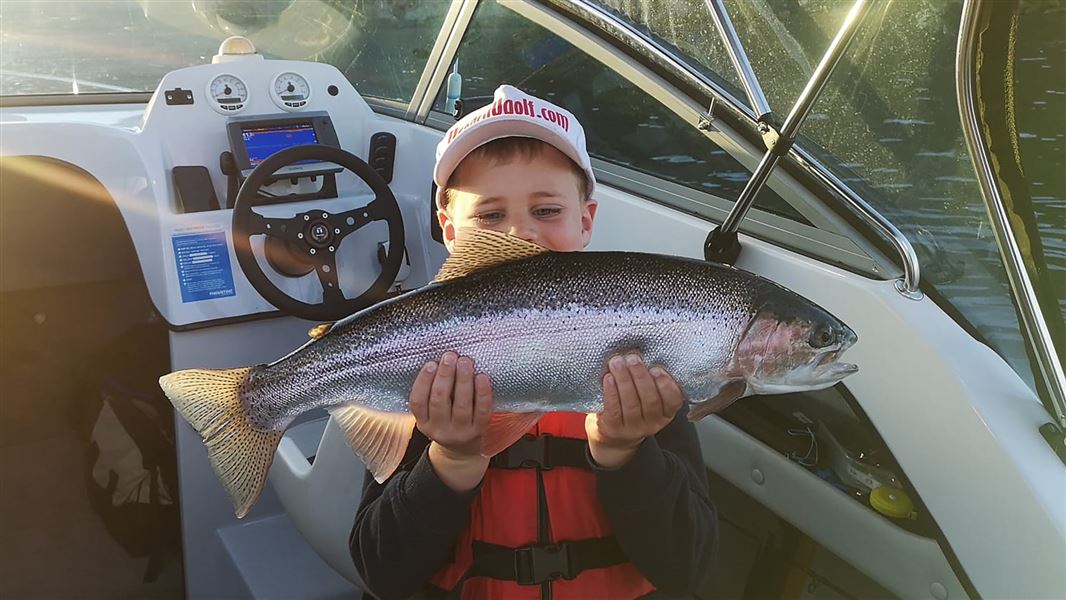 Young boy on a boat holding a caught trout. 