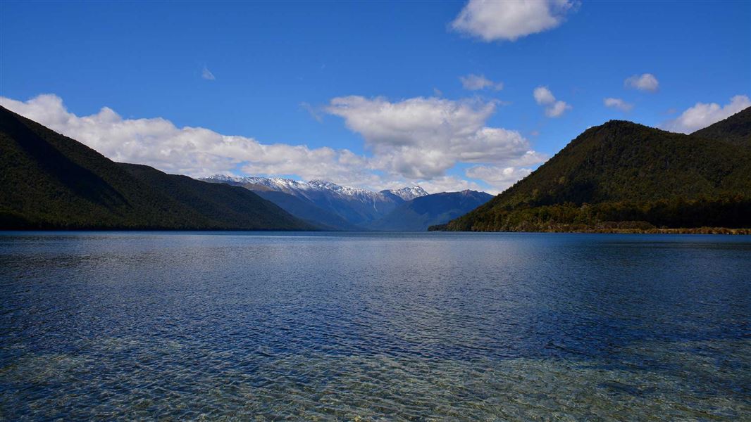 A clear blue lake stretches into the distance of a green mountainous valley.