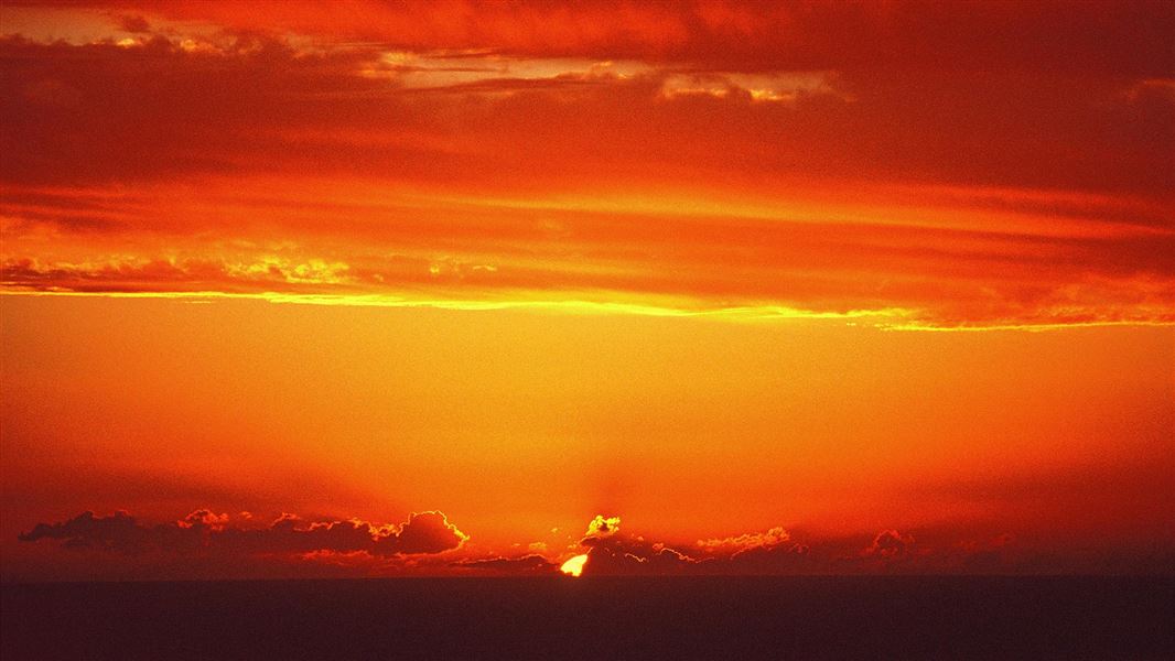 An orange sky as the sun set through clouds into the ocean.