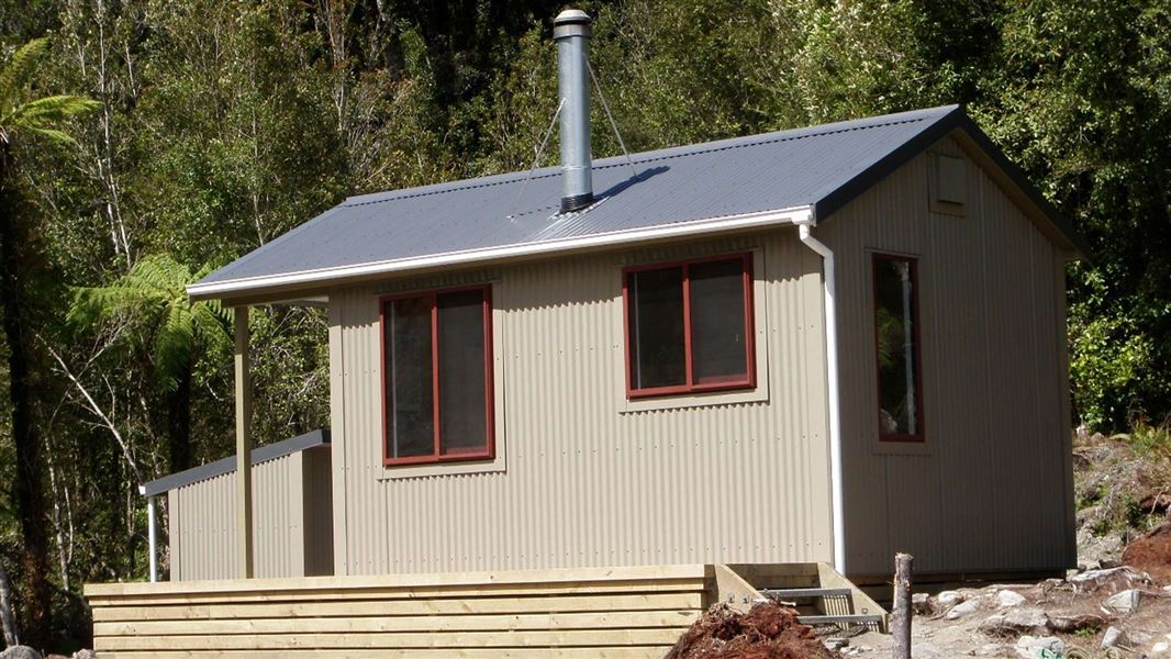 A beige corrugated hut with red aluminium framed windows and a small wooden deck. 