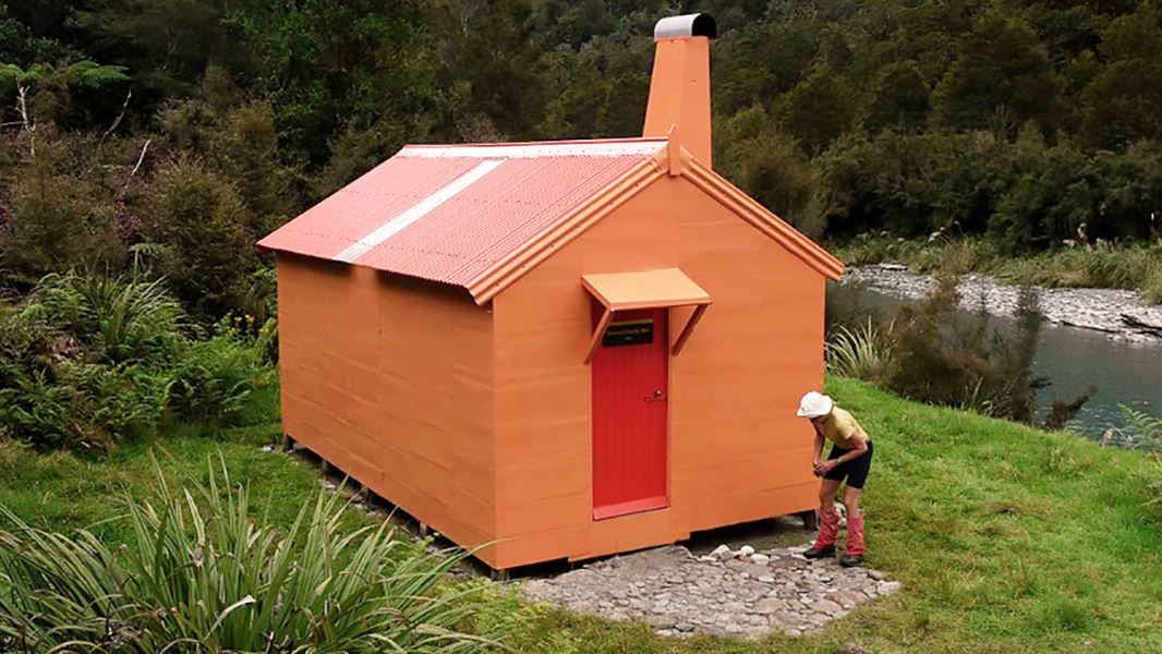 An orange hut with a chimney by the river surrounded by dense forest