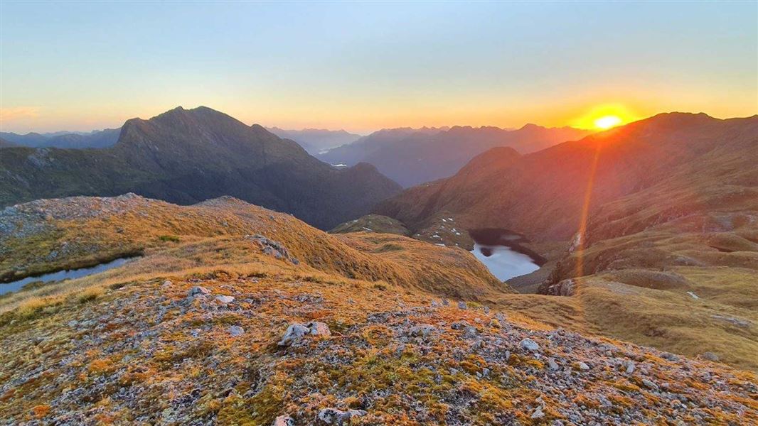 Fiordland National Park landscape featuring a deep blue lake or fiord surrounded by steep forested mountains beneath scattered white clouds.