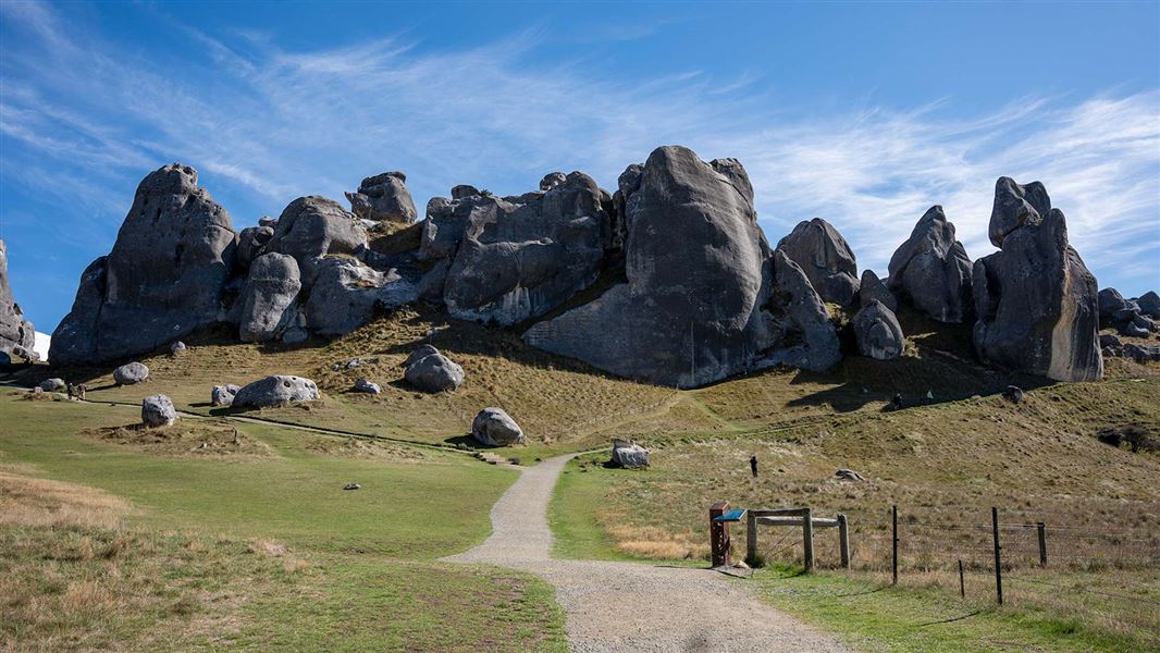 A track in an open field leading to looming rounded rocks. 