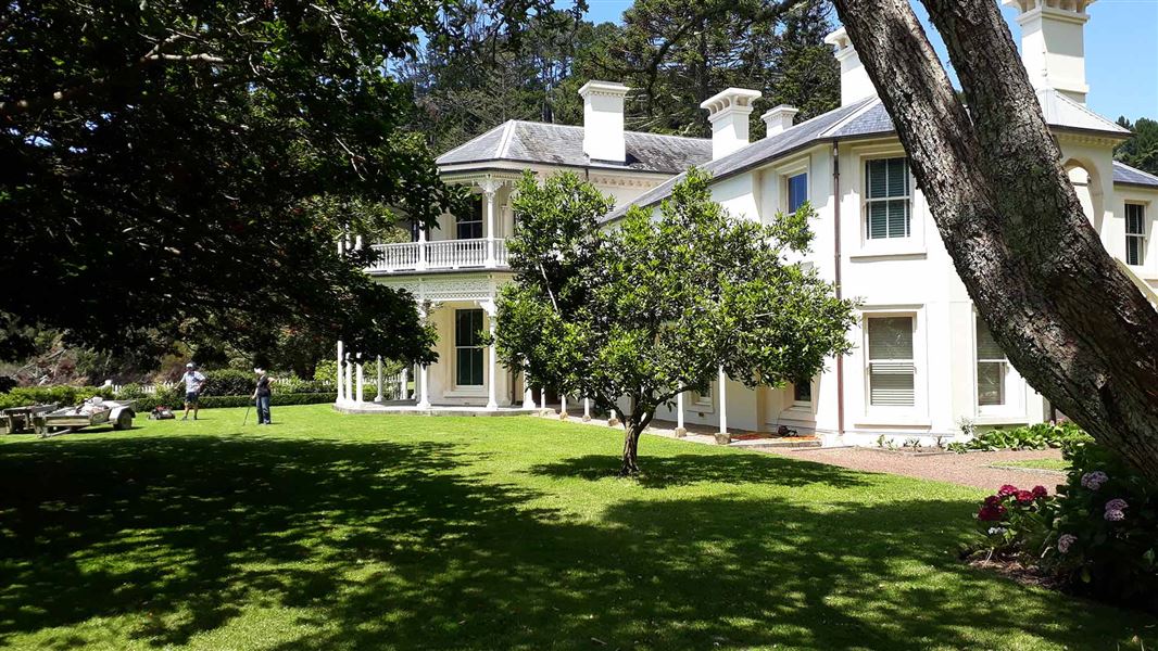 A view of Mansion House with some people standing on the lawn with gardening equipment.