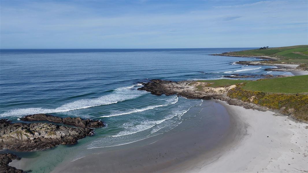 Beach landscape with flat sand, gentle waves and green land around it. 