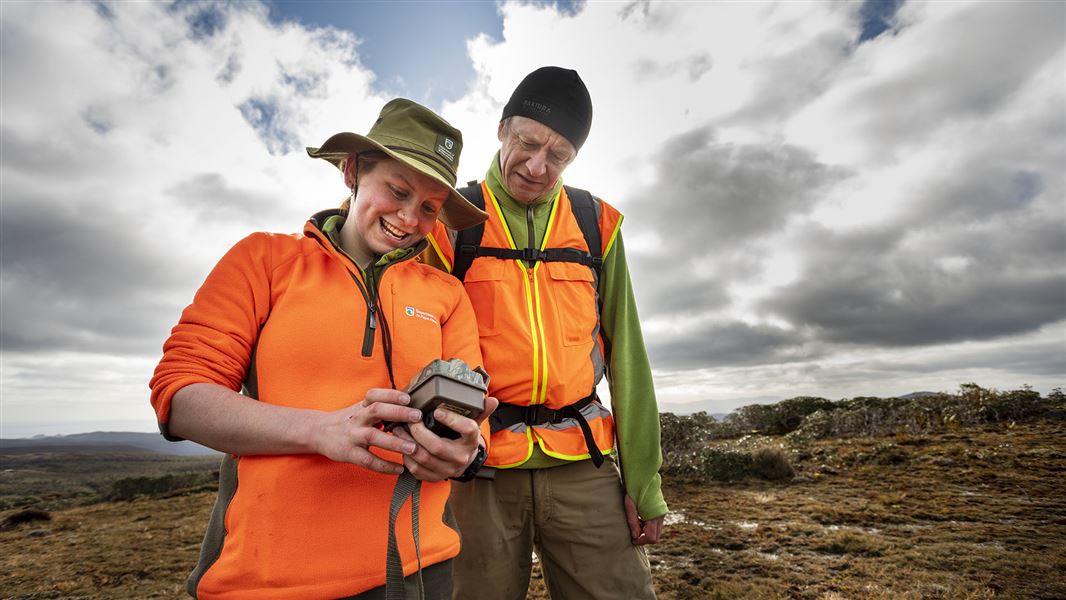 Two people standing together outside looking down at an electronic device.