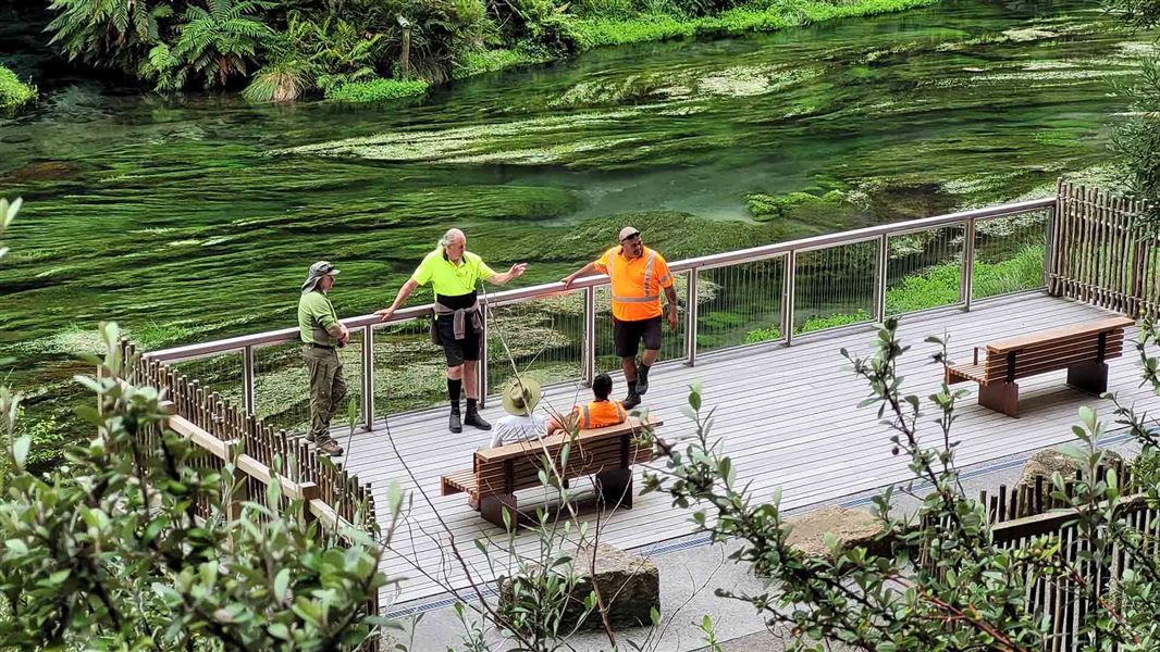 Five men in work clothes confer on a riverside viewing plaform.