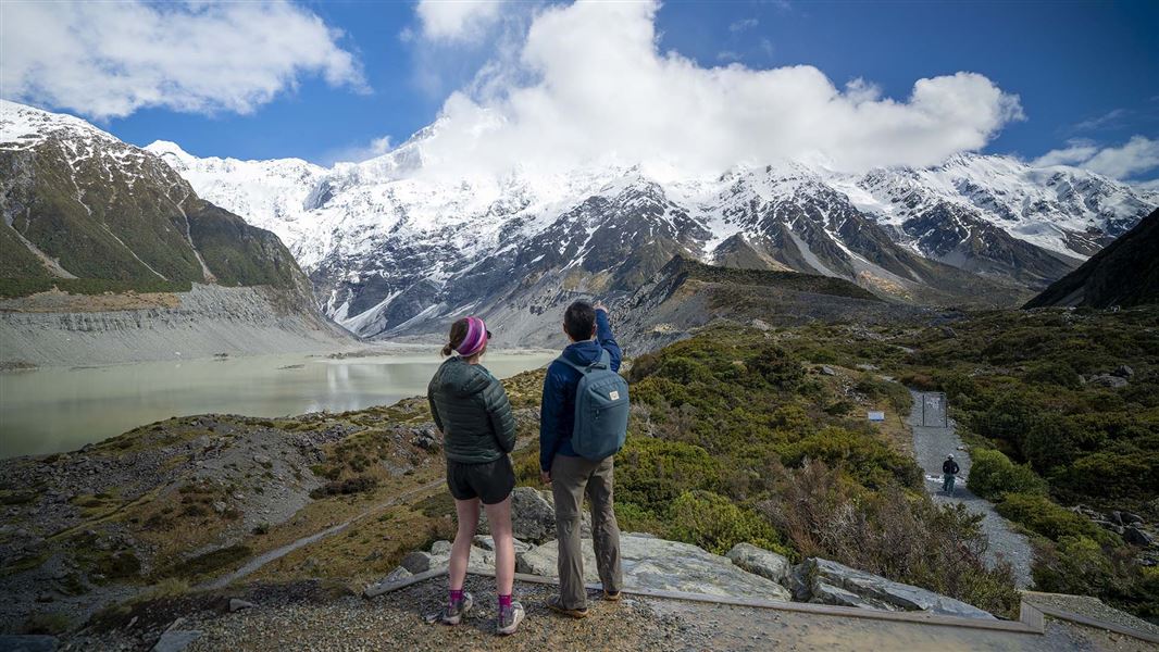 Two people admire a view of mountains and lakes.