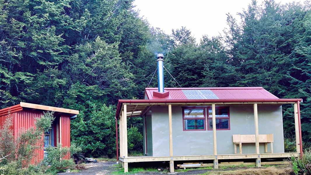 Hut and small outbuilding nestled in the trees.