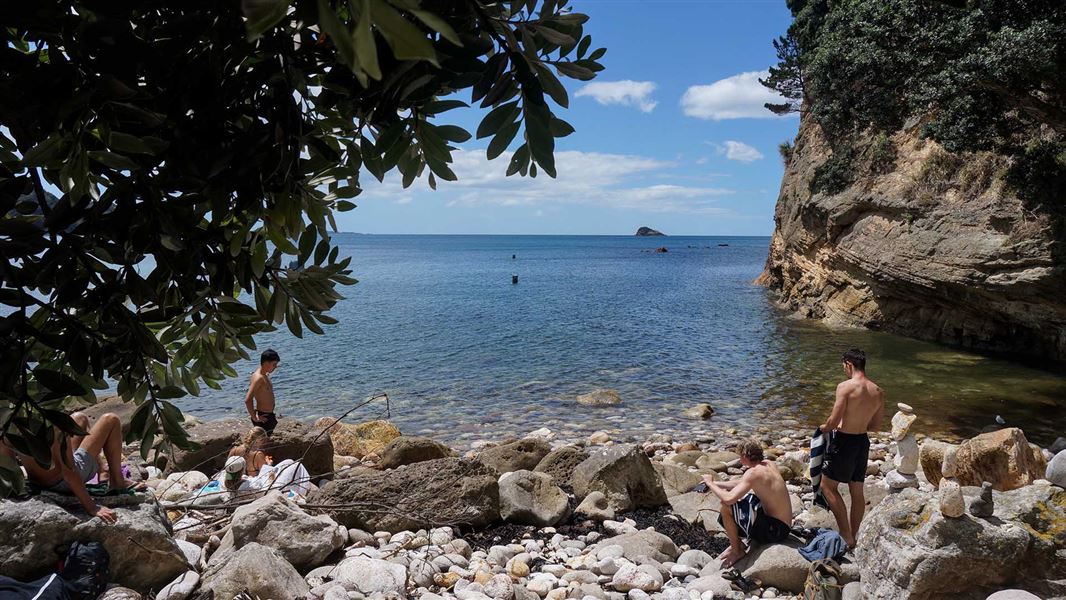 A group of sunbathers sitting on a rocky shore.