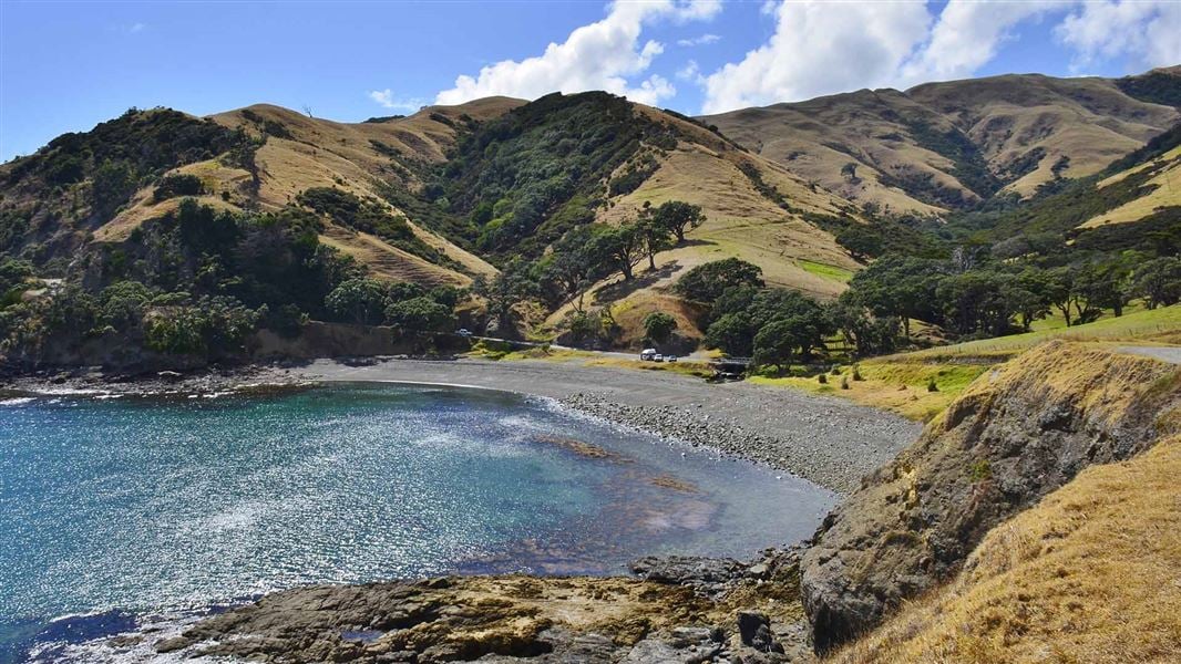 A view from up high of a stoney beach surrounded by partly forested hills.