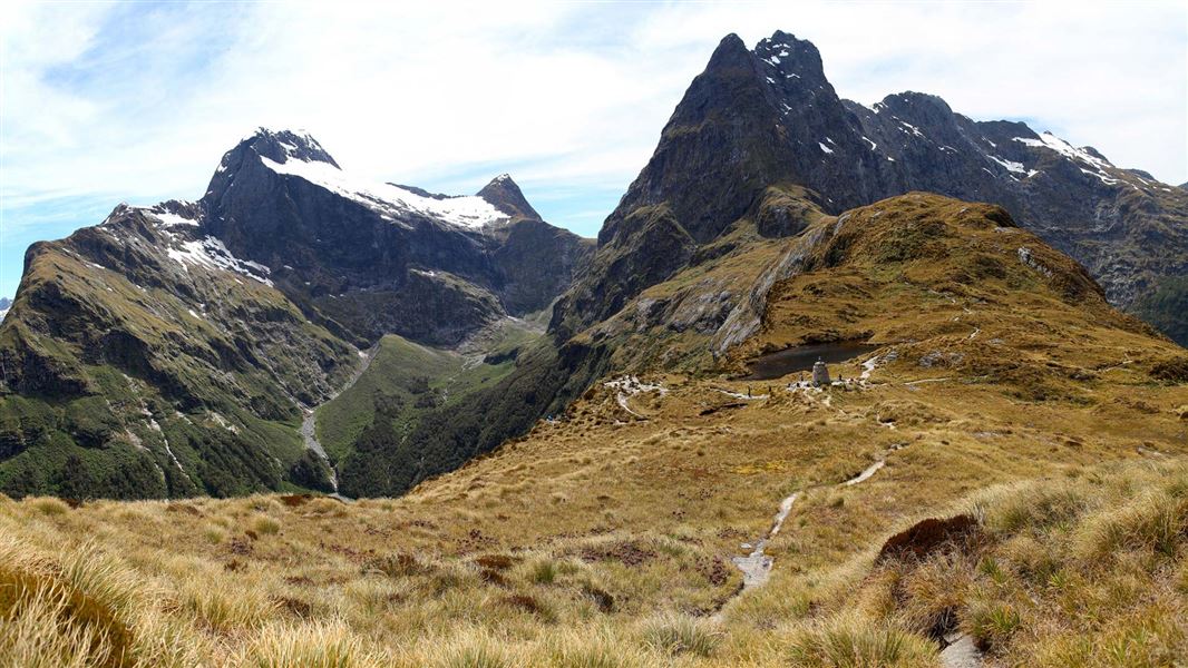 Tussock covered hills with high jagged mountains looming above. 