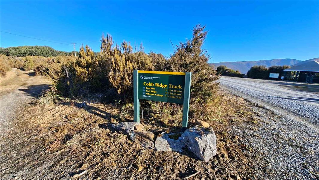 A wayfinding sign with destinations and distances stands lonely beside a gravel road. 