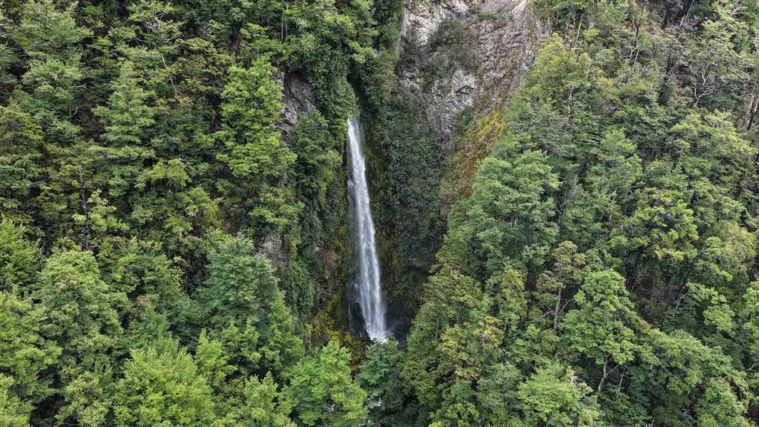 A high waterfall flows out from a cliff face.