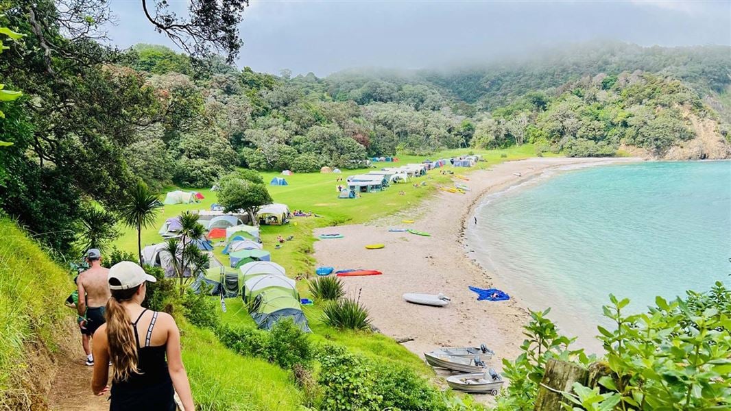 People walk down a track leading to a campground nestled in a bay.