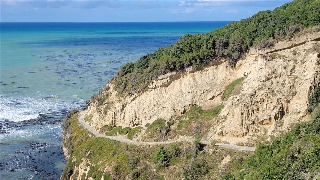 A pathway leads down and around a cliff face above a frothy sea.